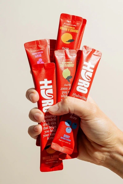 A high-contrast, close-up shot showing a hand clutching multiple brightly colored electrolyte drink mix sachets, emphasizing brand personality and variety.